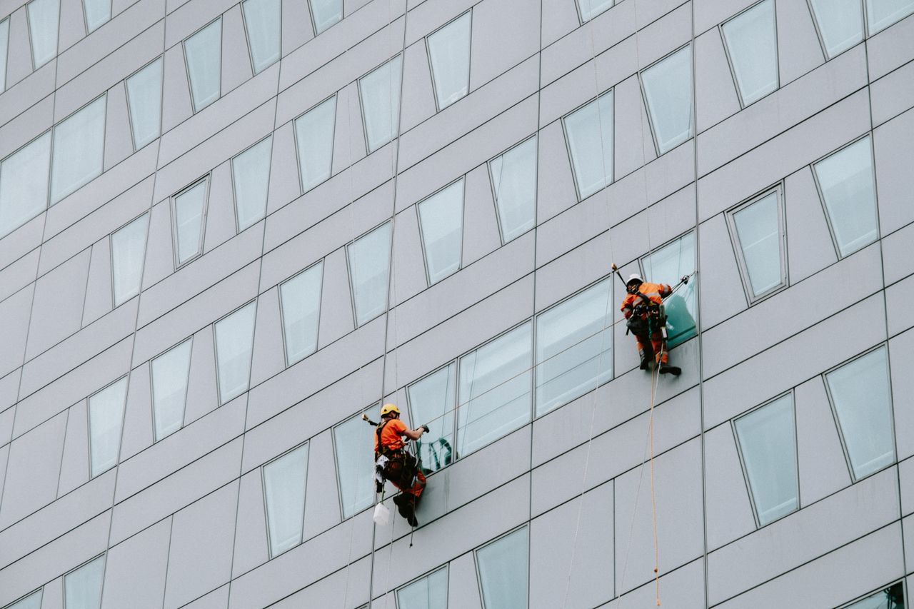 who-we-are High-rise window washers in safety gear cleaning a skyscraper facade.