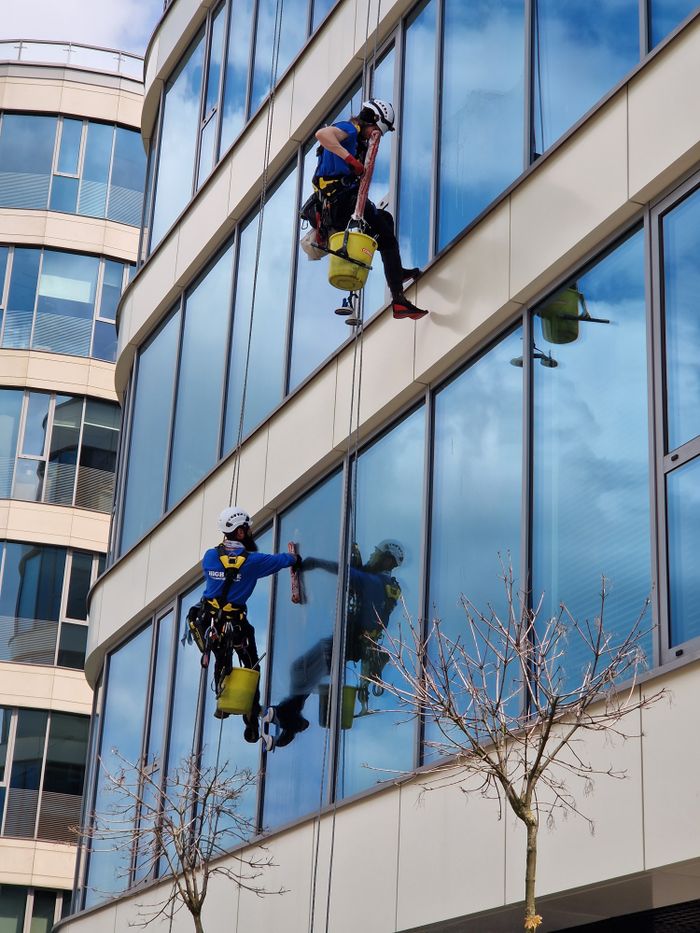 journey Two window cleaners using ropes on a modern skyscraper, showcasing urban professional maintenance.