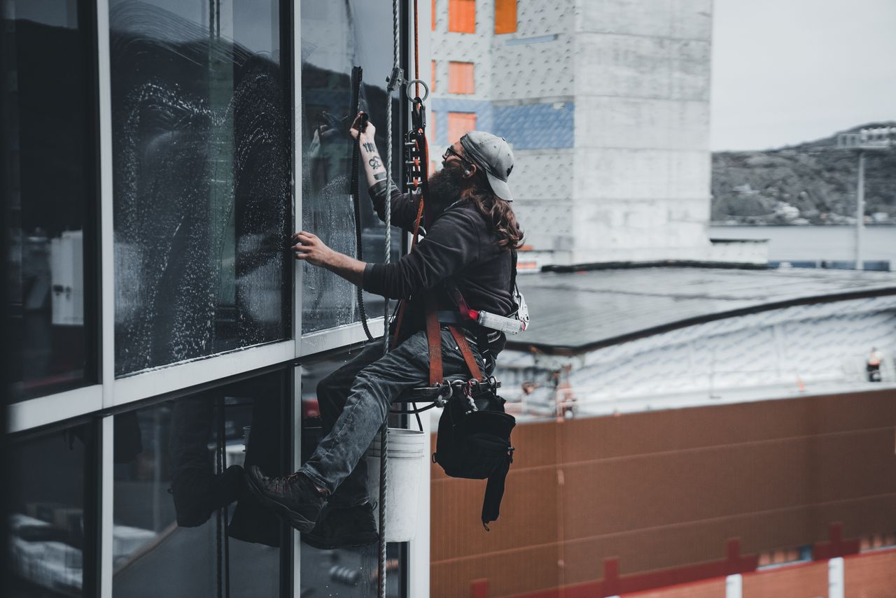 why-choose-us A man cleaning skyscraper windows with a harness, showcasing urban high-rise work.