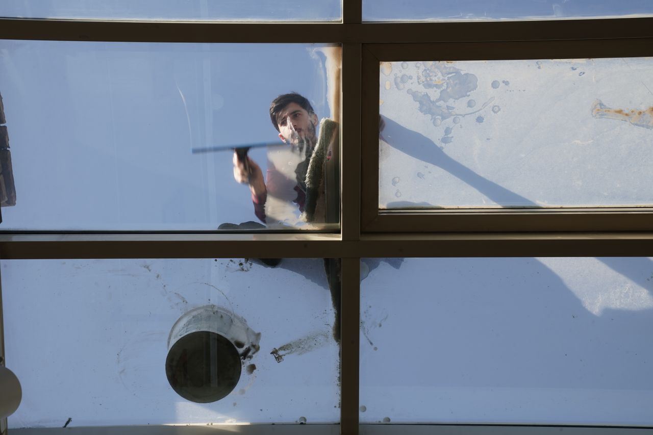 services-04 A male window cleaner washing the exterior glass roof from above with a tool during daylight.